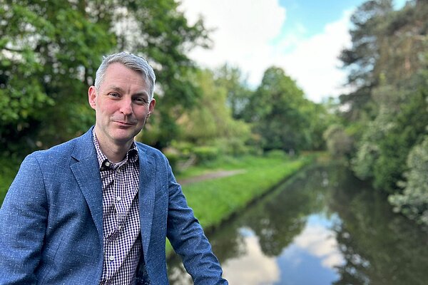 Will Forster wearing a blue jacket, in the background the river stretches away into the distance.