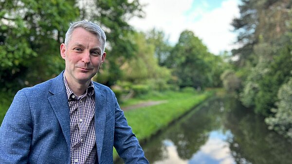 Will Forster wearing a blue jacket, in the background the river stretches away into the distance.