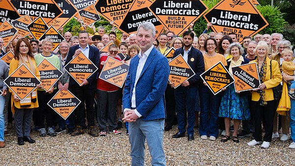 Will Forster stands in front of a crowd holding Liberal Democrat diamond signs